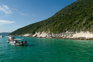Forma&ccedil;&atilde;o rochosa a beira-ma com muita vegeta&ccedil;&atilde;o, c&eacute;u azul e pequena embarca&ccedil;&atilde;o no mar, localizada na regi&atilde;o de Cabo Frio, Rio de Janeiro, Brasil.
