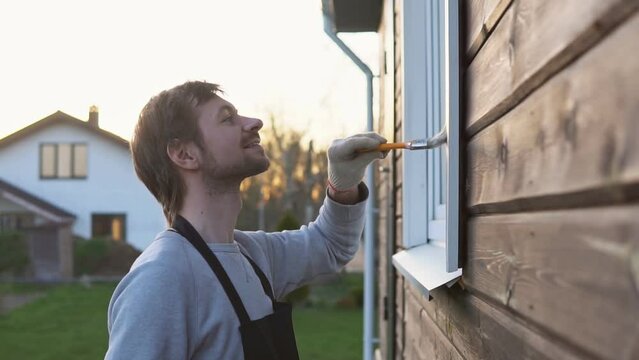Young man painting window with paint brush at home, closeup