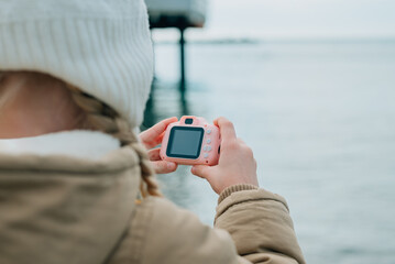 close-up of childrens hands holding a baby pink camera. the child is passionate about his hobby: photography, photographing the autumn, spring seascape