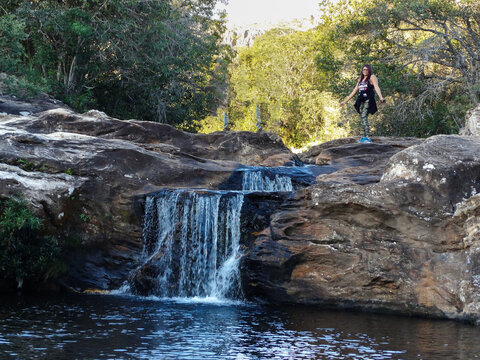 Pequena Cachoeira entre pedras, com muita vegeta&ccedil;&atilde;o em volta e mulher passeiando, localizada na regi&atilde;o rural de Tr&ecirc;s Barras, munic&iacute;pio do Serro, Minas Gerais, Brasil.