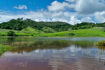 Vista de fazenda, com lindo lago artificial, céu azul, muita vegetação e montanhas ao redor, localizada na região rural do bairro Jardim das Oliveiras, município de Esmeraldas, Minas Gerais, Brasil.