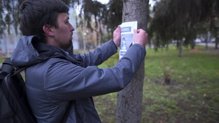 The man has lost his best friend a husky puppy. The owner posts an ad banner about the missing dog on the trees in the park. Missing pet banner. Dog search reward. Stole a pet. Lost Siberian Husky.