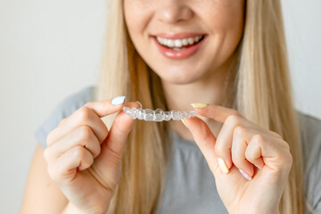 Close up of clear aligners in hands of happy girl who is standing and showing orthodontic device to...