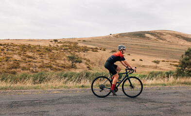 Fototapeta na wymiar Side view of professional female cyclist in sportswear riding pro bike against beautiful landscape