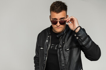 Obraz premium Cool trendy handsome man in a trendy black leather jacket wears sunglasses in the city