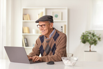 Happy elderly man sitting at home on a sofa with a laptop computer