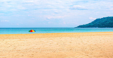 Fototapeta na wymiar Tropical sandy empty beach on an island in Thailand with a bright colorful sun umbrella in the sand. Travel and tourism. Panorama with place for text