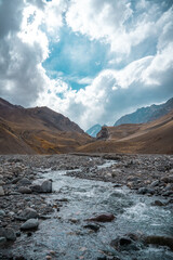 Vertical shot of rushing river in rocky valley in Cajon del Maipo with mountains in the background on a sunny day, Chile