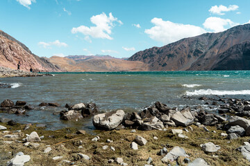 Horizontal shot of the shore of the Embalse del Yeso reservoir with rocks, moss and turquoise water, Chile.