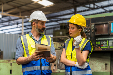 Young man and Young woman are discussing in industrial plants. Engineer with clipboard and tablet on hand to see how the machine works.