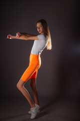 Pretty sports girl with short orange leggings posing isolated on dark background in studio