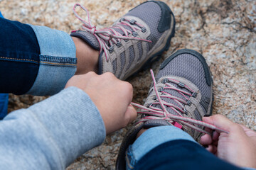 Close up shot of a woman tying her shoes in the mountain. Young girl tying her shoelaces of his...