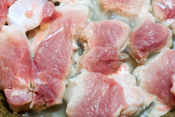 Pieces of pork are fried in a frying pan. Closeup