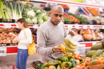 Buyer selects ripe bell peppers in the vegetable section of the supermarket