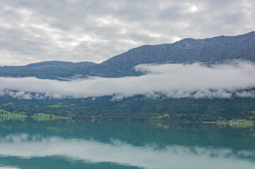 Fototapeta na wymiar View of the Lustrafjord in Norway. turquoise sea water, low white clouds above it, cloudy sky, green forest on the mountain slopes