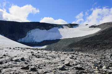 Norwegian landscape with snow covered melting mountain glacier and blue sky with clouds. 