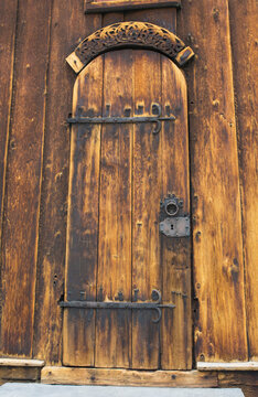 Carved doorway of the medieva lviking Lom stave church in Lom, Norway. Shabby brown and yellow timber and black forged iron lock and hinges
