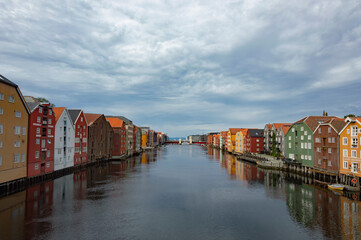The Nidelva river flowing through the Trondheim city in Norway. Colourful old wooden storehouses on the river bank, grey water, cloudy sky