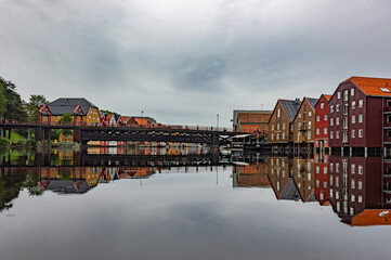 Fototapeta premium The Nidelva river flowing through the Trondheim city in Norway. Old wooden storehouses on the both river sides, old town bridge grey water, cloudy sky, 