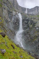 Mardalsfossen waterfall in Norway. White water stream, grey rocky mountains, green grass, clouds of the water dust