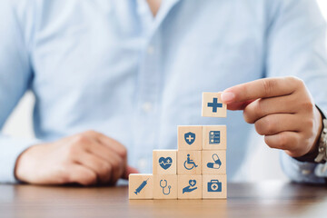 Man in blue shirt is arranging wooden blocks with healthcare medical icons on white background. health care and health insurance concept