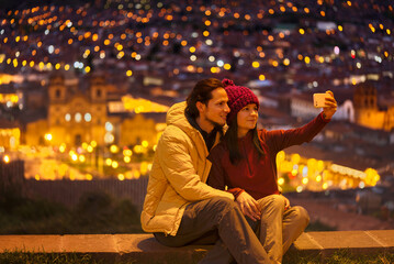 Pareja de turistas sentados en el mirador tomándose un selfie hacia la plaza de Cuzco