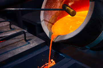 Pouring molten metal from a ladle into a rectangular graphite mold.