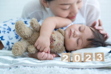 Close up, Happy attractive young mother with her 6 month old daughter sleeping, and number 2023 wooden block, selective focus