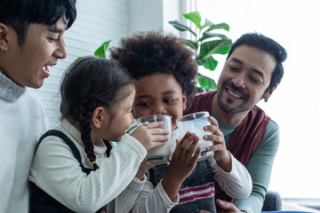 Lgbtq father and mother cheer for son and daughter drinking milk in a glass, having fun with kids at home, Lgbtq family concept