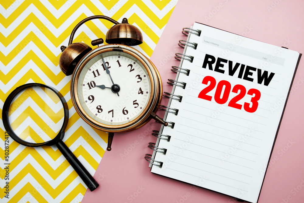 Poster review 2023 text on paper notebook with alarm clock top view on pink background