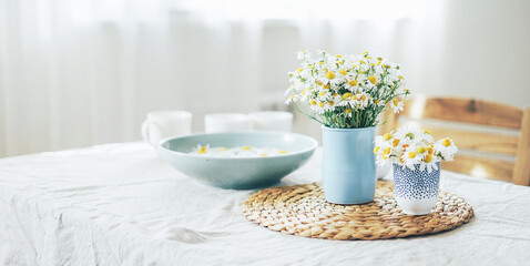 Table with flowers chamomile on linen tablecloth in living room, banner