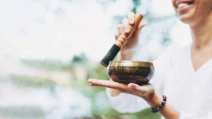 Young smiling woman playing on the brass Tibetan singing bowl outdoor, banner