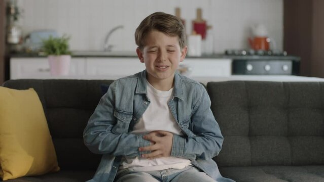 Little boy suffering from stomachache while sitting on sofa at home.The child has a stomach ache.