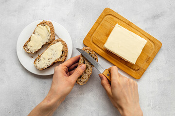 Hands spreading butter with knife on toast bread. Top view