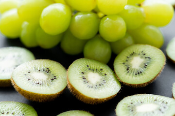 close up view of green grapes and sliced fresh kiwi on black.