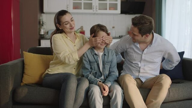 Birthday and happy family portrait.Portrait of happy modern parents giving a soccer ball to their son as a birthday present.Young mother closes her son's eyes and surprises his father.