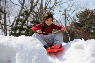 雪の坂でそり遊びをする女の子