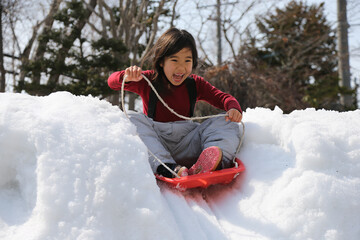 雪の坂でそり遊びをする女の子