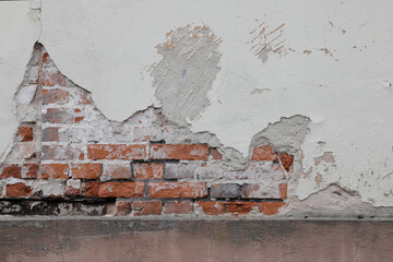 White painted stone wall with cracked surface, bricks under cement, no person