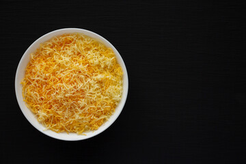 Shredded Mexican Cheese Mix in a White Bowl on a black background, top view. Flat lay, overhead, from above. Copy space.