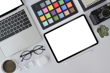 Creative designer workplace with digital tablet, laptop, camera and color swatch on white office desk.