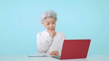 パソコンを見ながらメモを取るシニア女性　オンライン授業