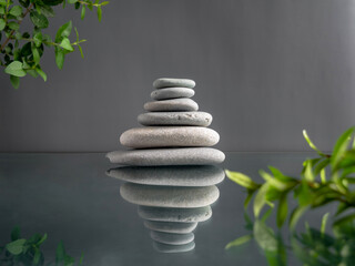 A pyramid of flat stones is depicted on a gray background. Zen stones. Reflection of stones. Green branches. The concept of harmony, meditation, peace. Horizontally. Place for text