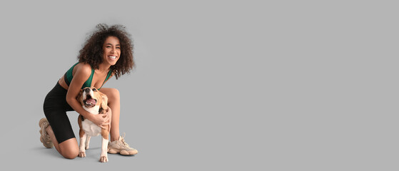 Sporty African-American woman with cute dog on grey background - obrazy, fototapety, plakaty