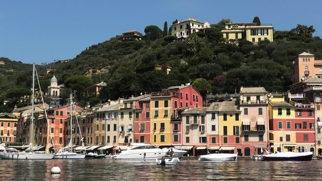 Shot of quiet fishing village Portofino, Italy facing houses and mountain with small boats in de harbour