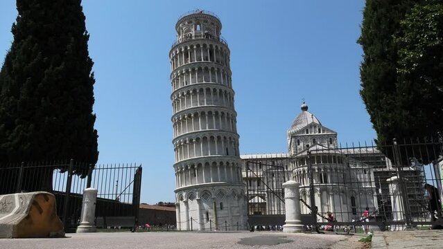 Quiet scene of the Leaning Tower of Pisa leaning to the left with fence in front and few people