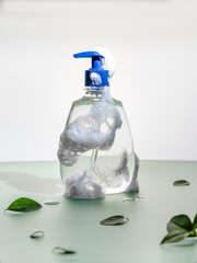 Soap dispenser with foam around the package. The concept of cleanliness and washing. There are green leaves nearby. Hand care concept with natural ingredients. White-green background. Side view. Place