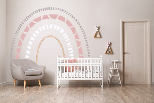Interior of children's room with crib, armchair and light wall with painted rainbow