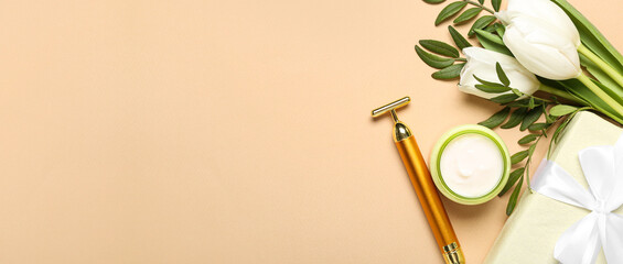 Facial massage tool, cream, gift box and tulips on beige background with space for text. Mother's Day celebration