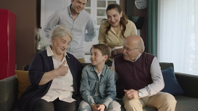 Happy family portrait. A scene where a young couple gives flowers and a gift box to their elderly parents. The extended family celebrates a birthday, holiday, mother's day or father's day.